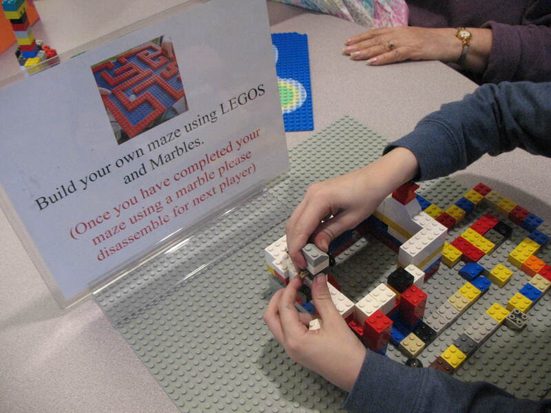 A child's hands are building a simple, multicolored maze out of LEGOs.