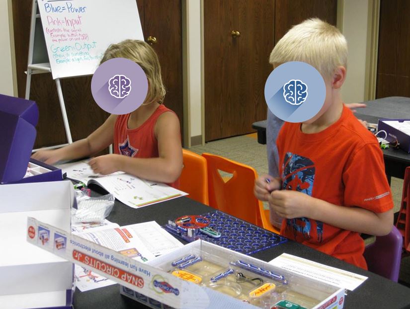 Two excited children construct a connection of  switches, snaps, lights, and buttons. 